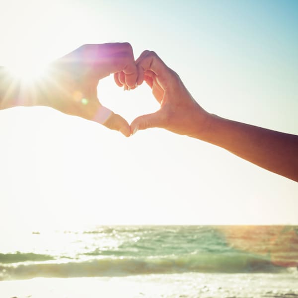 Zwei Hände formen ein Herz am Strand